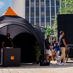Black dome-shaped promotional tent beside a branded event trailer in an outdoor plaza