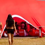 People entering a large red Coca-Cola-branded event tent on grass