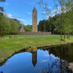 Sunlit grounds and stone tower reflected in the water at Glenpark Estate, Omagh